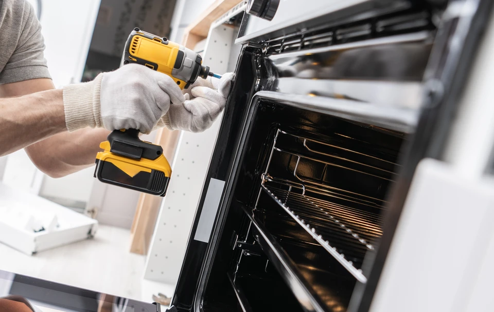 Cuisine moderne avec ouvrier en uniforme rouge installant électroménager encastrable blanc dans meuble bas gris anthracite