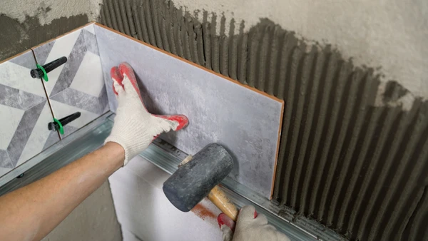Professionnel en salopette bleue installant un parquet stratifié dans une pièce moderne aux murs blancs et gris